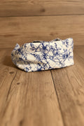A small fabric pouch with a blue floral print on a cream background, resting on a rustic wooden surface.
