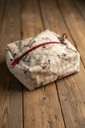 A small fabric zippered pouch with a chicken print pattern on a light background, featuring a red zipper and red tassels, resting on a blue surface.